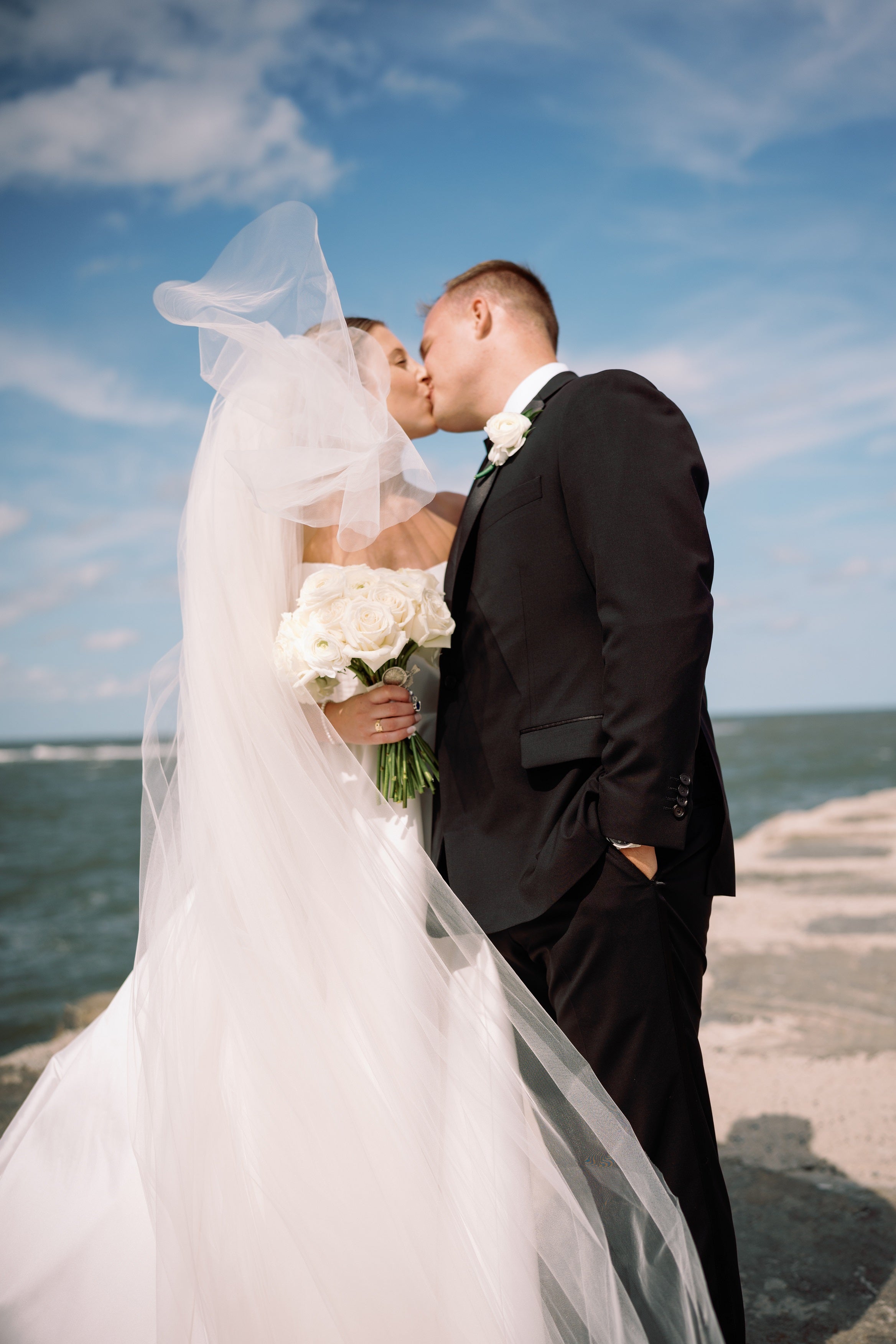Newly married couple kissing on a beach with a clear blue sky after wedding ceremony at the Jersey Shore.